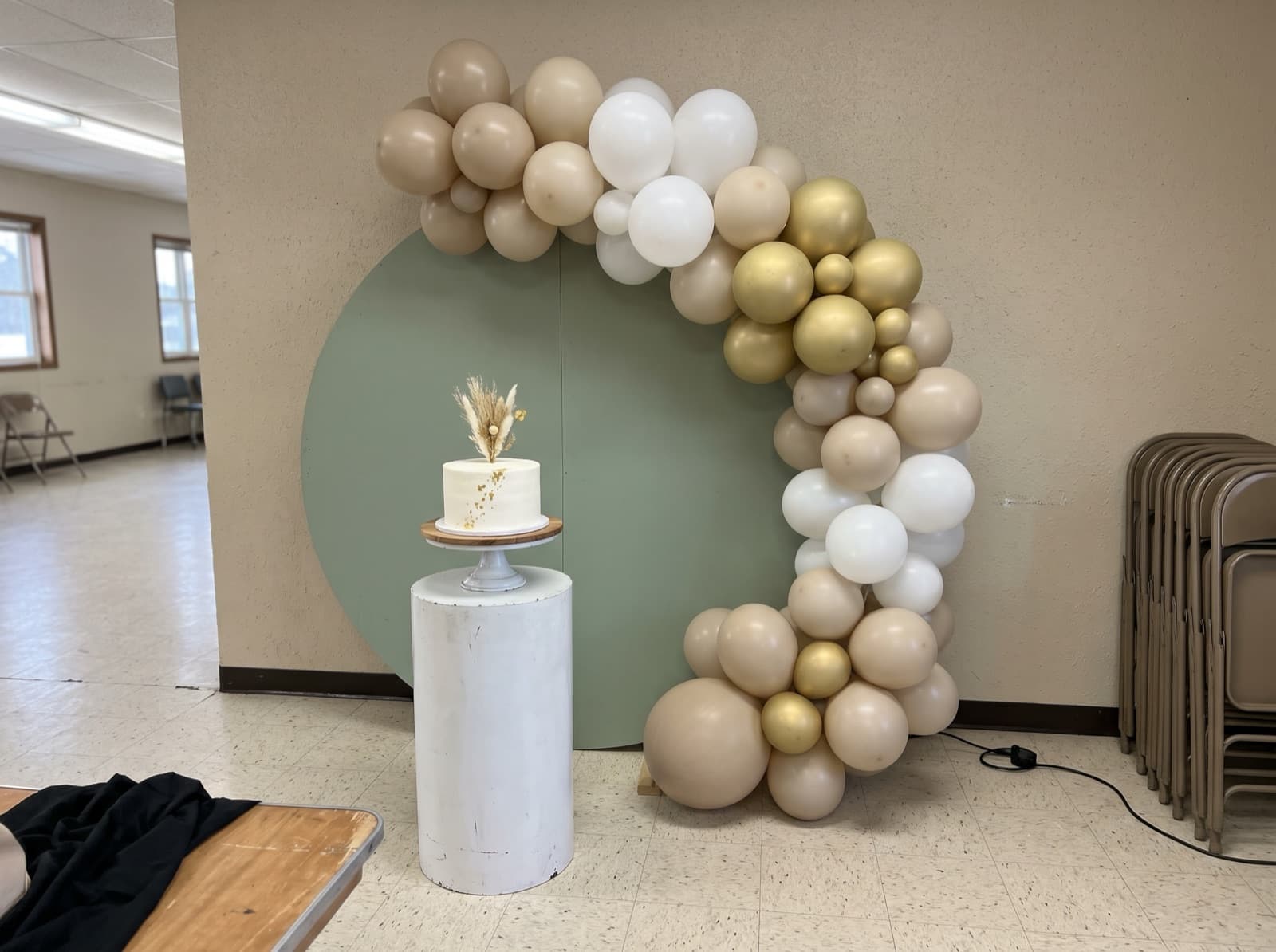 Round sage backdrop with a sand and white organic balloon garland and a cake stand at a birthday party