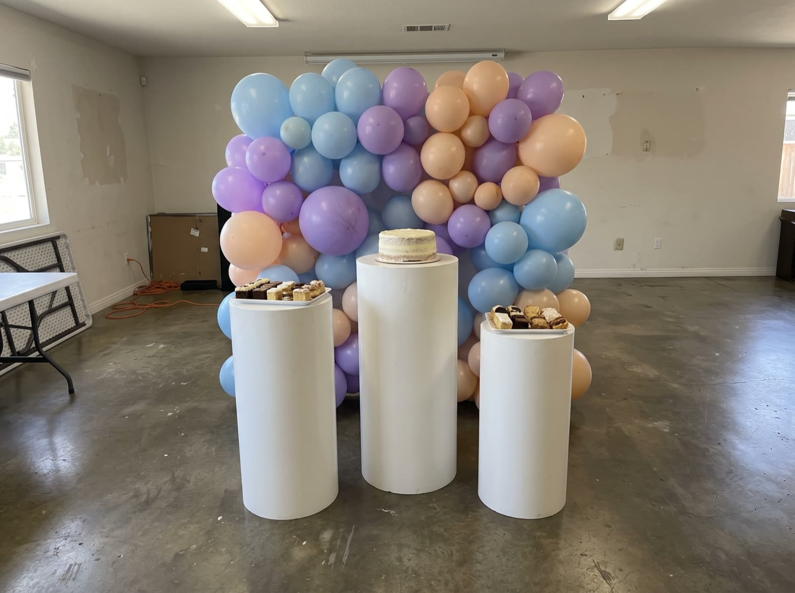 Balloon backdrop with pedestals and a cake