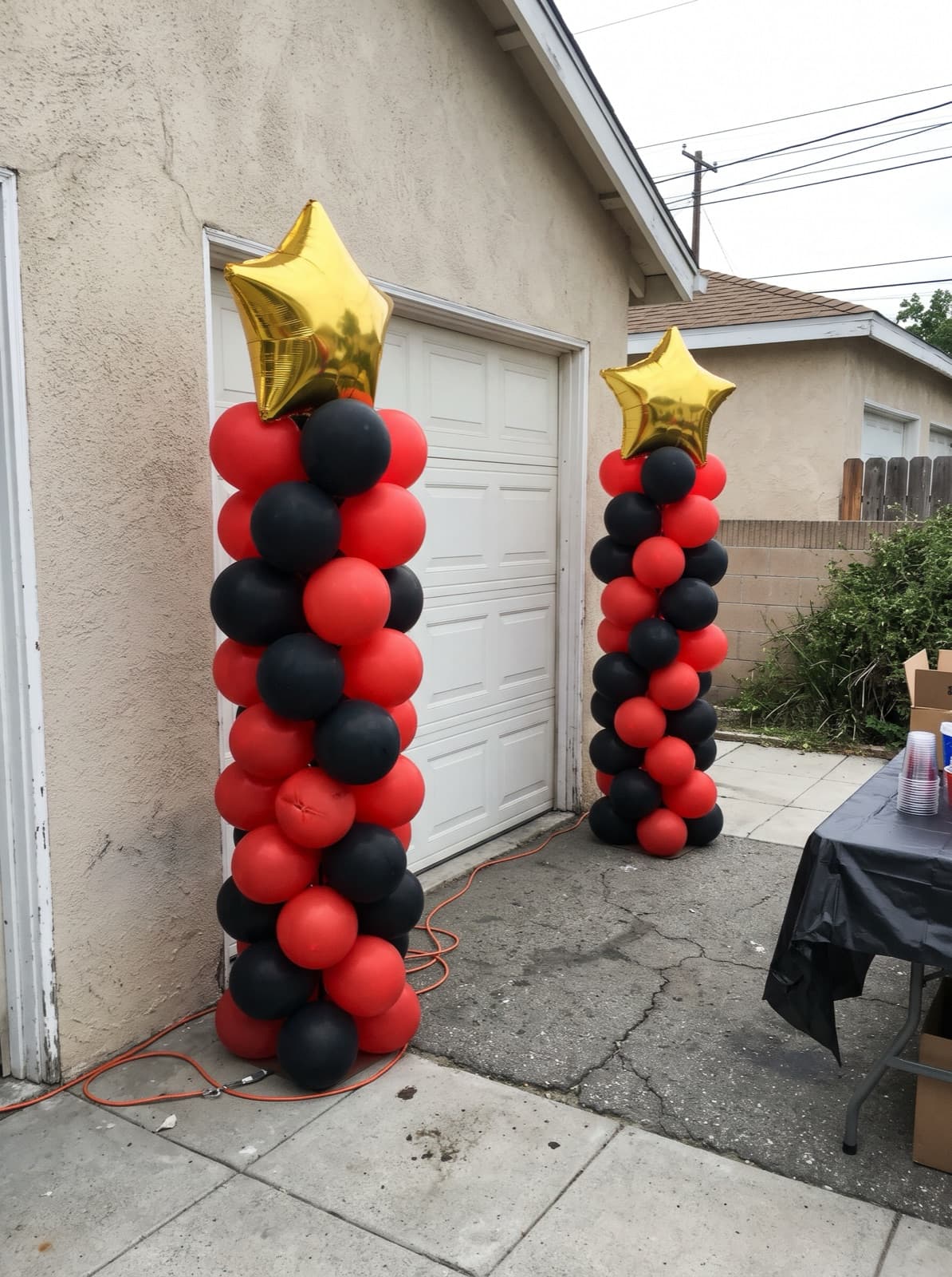 Pair of spiral balloon columns in scarlet and black with gold star toppers at a backyard graduation party