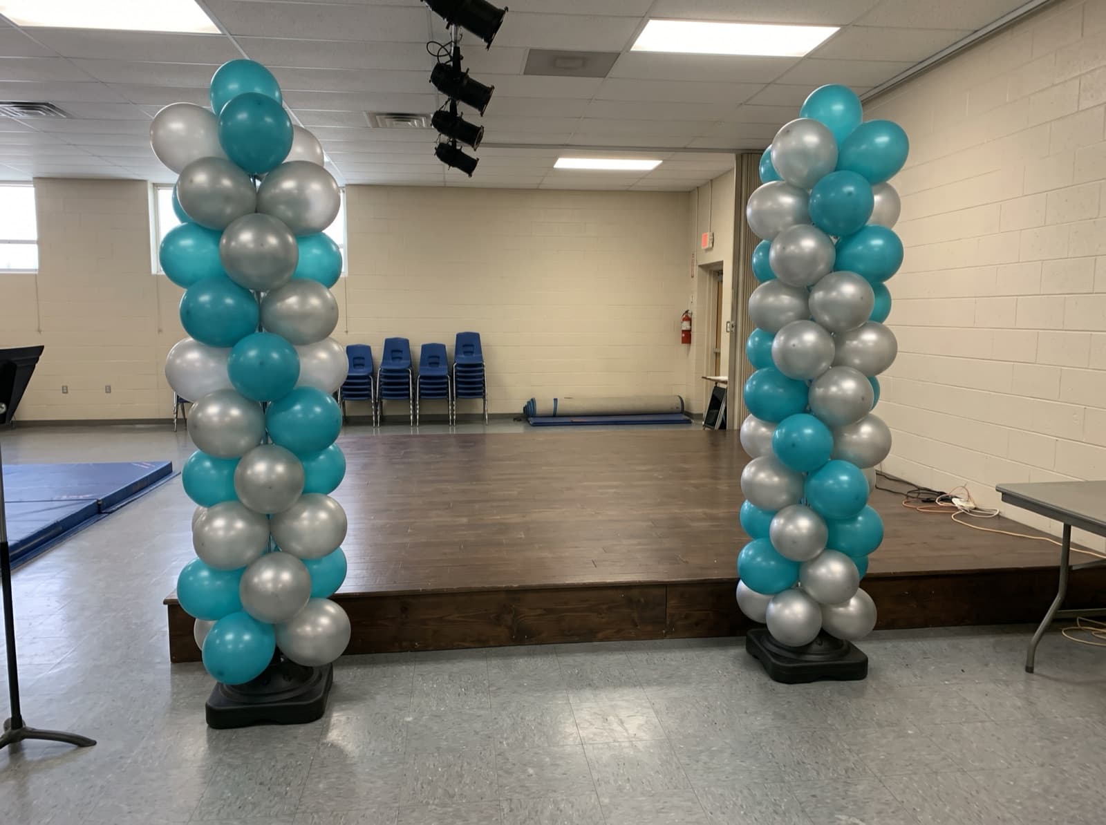 Tall teal and silver balloon columns on each side of a stage
