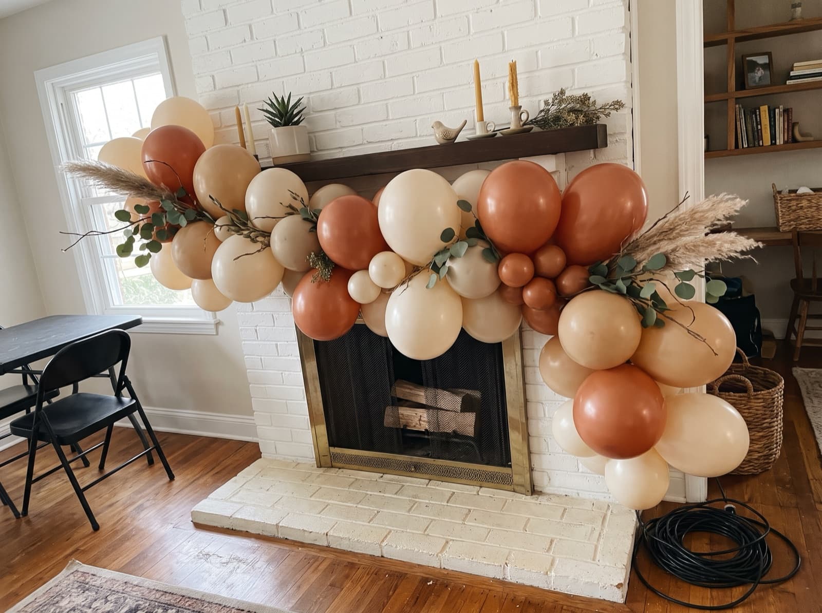Organic balloon garland in terracotta, sand and ivory along a fireplace mantel in a San Diego living room